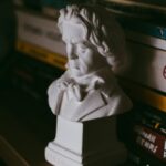 Plaster bust of a figure displayed on a bookshelf with dim atmospheric lighting.