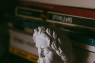 Plaster bust of a figure displayed on a bookshelf with dim atmospheric lighting.