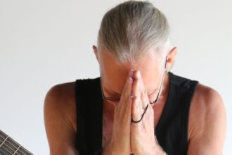 Man with acoustic guitar in prayer pose, conveying peace and introspection.