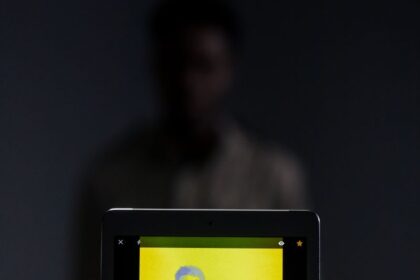A digital portrait of a man on a tablet screen with a dramatic yellow color filter.