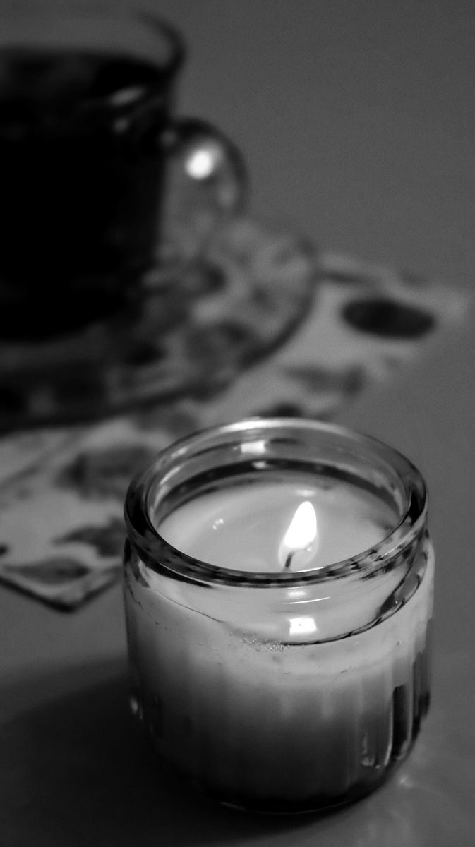 Black and white cozy scene with a lit candle next to a teacup, creating a warm atmosphere.
